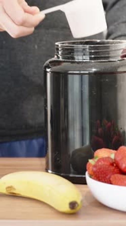 Vertical. A man prepares a sports protein drink, pours powder from a measuring spoon into a glass
