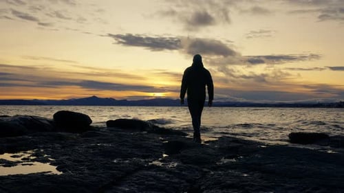 Mann spaziert am felsigen Seeufer gegen Sonnenaufgang über dem Horizont