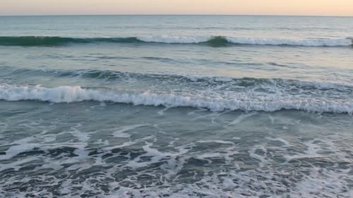 Gentle sea waves lap near the shore of the sea at sunset