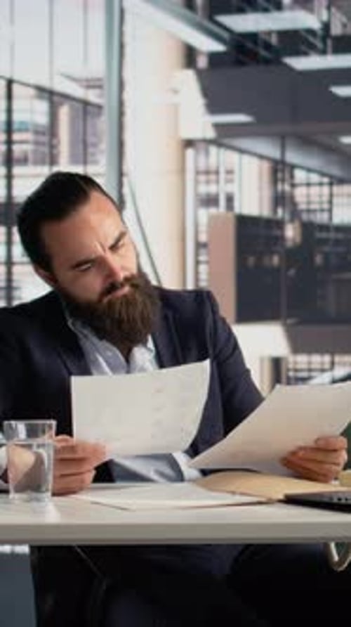 Vertical Video CEO Engaged in Reviewing KPIs on Documents and Laptop