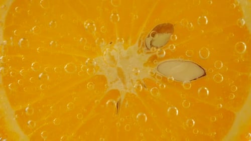 Eine Scheibe reifer Orange im Wasser sprudelt auf einem orangefarbenen Hintergrund.