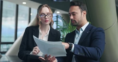 Happy business colleagues laughing while reviewing papers together in modern corporate office
