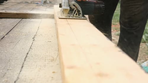 Male Carpenter Using Electric Circular Saw in Backyard Workshop with Wood Chips Flying Building