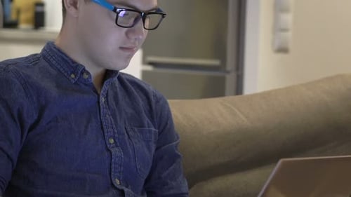 Teenage boy at home works on his laptop in the evening alone in apartment room