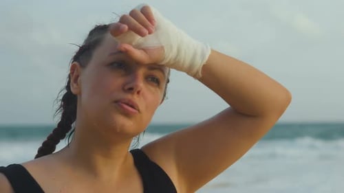 Boxeuse MMA Fighter essuyant la sueur du front sur la plage au coucher du soleil
