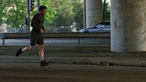 Athletic Young Man in Earphones and Sports Outfit is Jogging in the Street. He is Running in an Urb