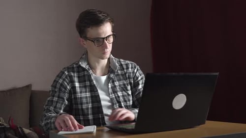 A Young Man Notes an Online Lecture in a Notebook