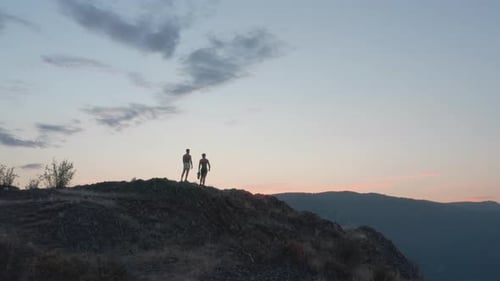 Silhouetted people view beautiful sunset landscape from top of mountain, aerial