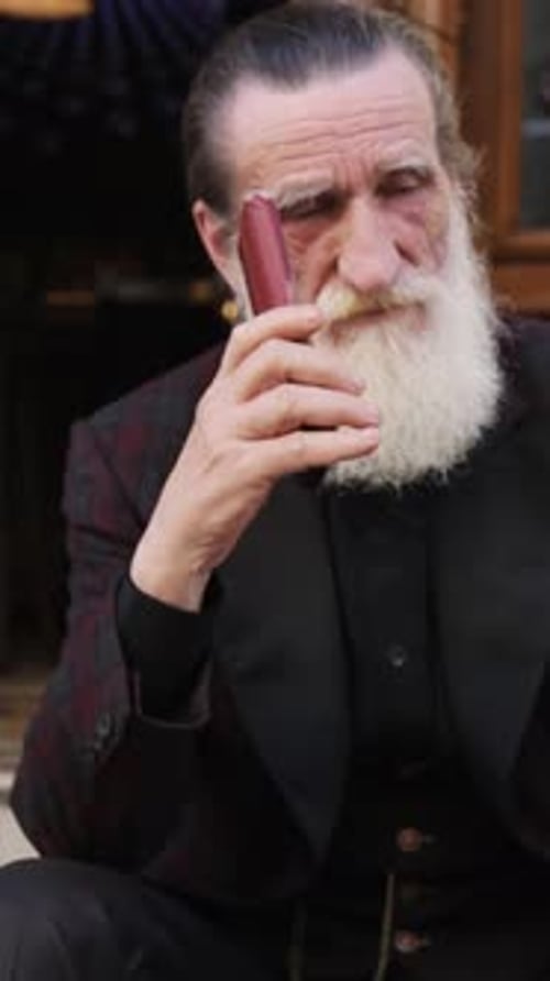 Elderly Man with a Long White Beard Sitting on Stone Steps and Holding a Red Hat in a Calm