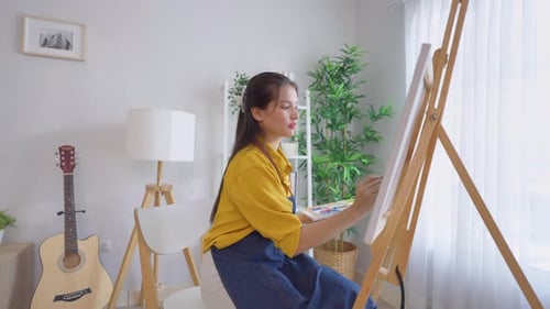Asian young talented woman artist coloring on painting board in house.