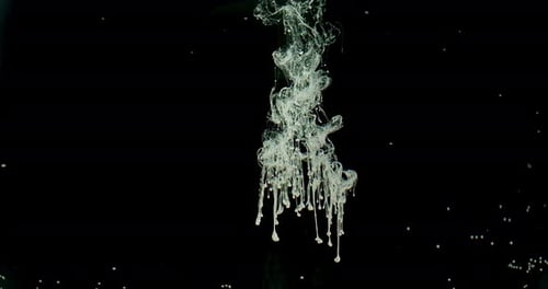 Des gouttes d'encre blanche se diffusent à l'intérieur de l'espace noir, abstraites