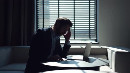 Stressed Man Rubs Temples at Desk in Darkened Room