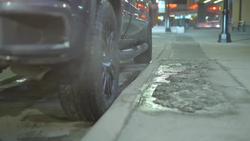 Close-up of the back wheels of a truck as it reverses into a parking spot next to a curb. Night time