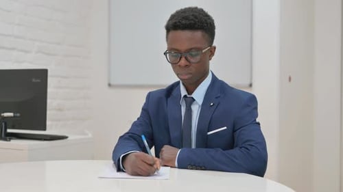 Young African Businessman Writing on Paper in Office