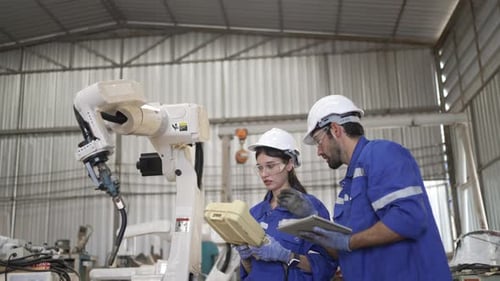 Blue collar workers at machine shop with welding robot arm.