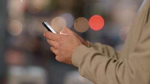 Closeup of businessman hands typing on phone in a busy city at sunset