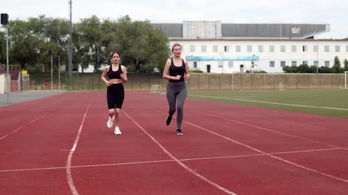Two Women Athletes Run Around Stadium in Sportswear and Shake Hands at Finish Line Front View Women