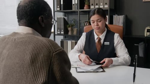 Bank Employee Handling Documents of Elderly Customer in Office