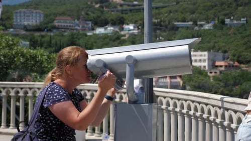 A Woman Looks Through Stationary Binoculars on an Observation Deck By the Sea