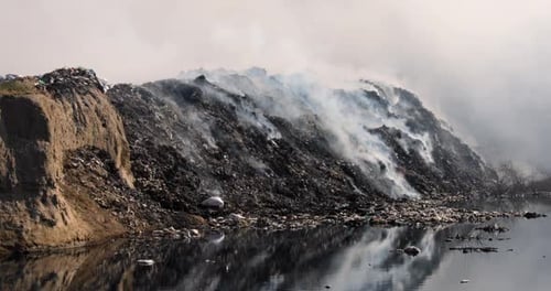 Smoking Landfill and Trash Heap by Polluted Water
