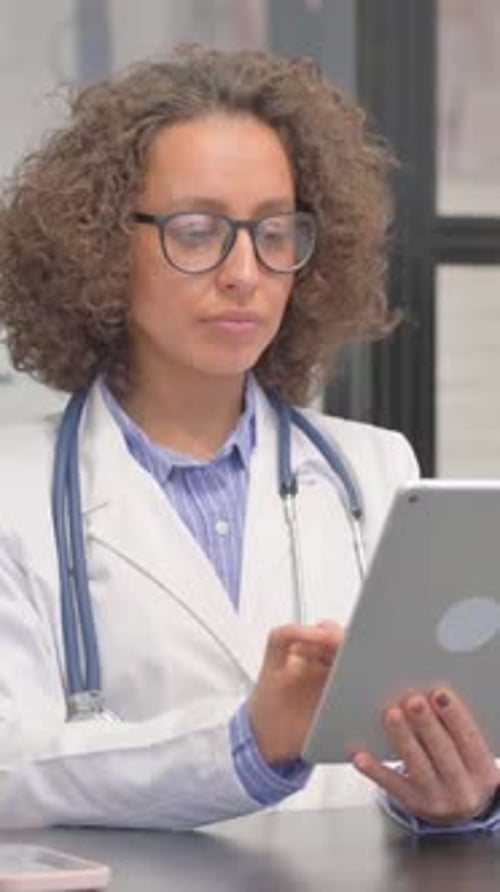 Vertical, Hispanic Female Doctor Doing Video Chat on Tablet in Hospital