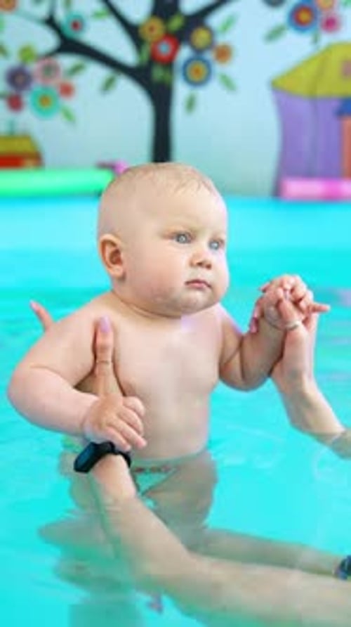 Female hands holding a little cute baby in the swimming pool. Lovely infant child learns to swim.