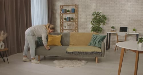 Woman cleaning grey sofa with yellow sponge indoors