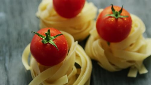 Fresh Tomato on Uncooked Pasta Nest on Wooden Table