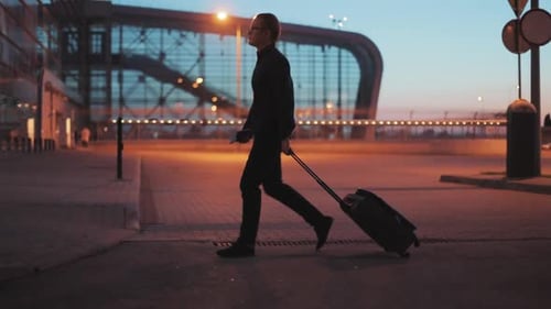 Attractive Young Man Pulling Suitcase in Modern Airport Terminal Wearing Smart Casual Style Clothes