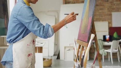 Video of biracial female artist painting in studio