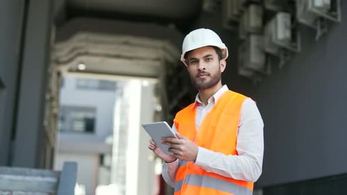 Portrait of smiling professional engineer wearing safety helme, vest standing at factory holding