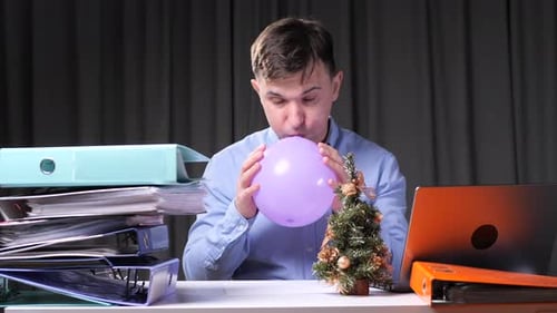 Office Worker Inflating Balloon at Christmas Time with Stack Folders and Laptop