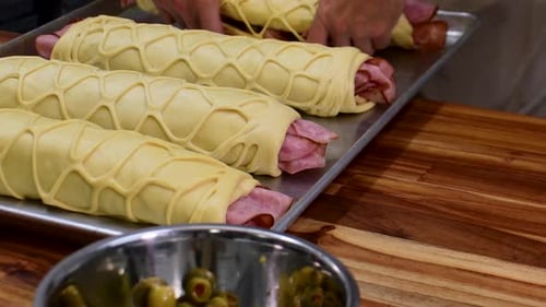 Ein festliches Schinkenbrötchen mit Oliven und Speck auf Holzoberfläche herstellen