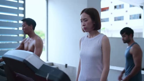 A young woman exercises in the gym by running on a treadmill with the assistance of a trainer.