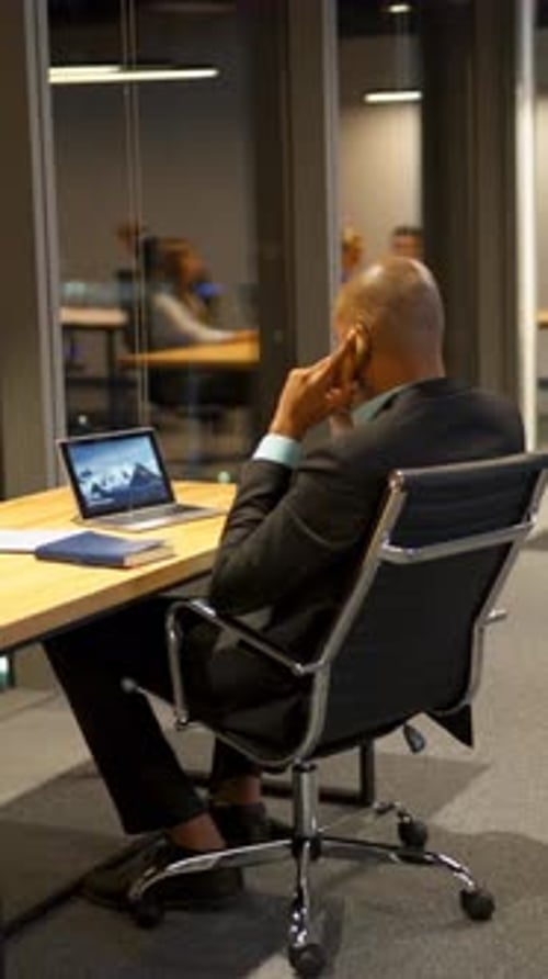 Vertical of Businesspeople Talking Discussing and Using a Laptops Tablets and Drawing at Office Desk