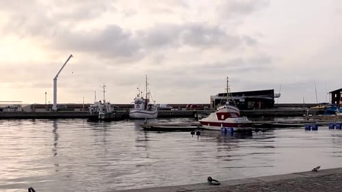 A few Boats Calmly floats on the Water in the Harbor while the Sun Sets behind some Clouds