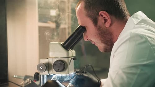 Man Using Microscope and Soldering Tool in Lab
