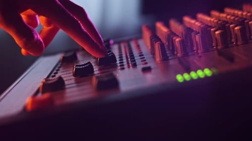 Sound Engineer Moves Faders Up and Down on Audio Mixer in Neon Light CloseUp