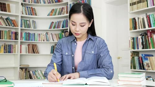 Asian female student studies taking notes doing homework in campus library space. Young beautiful