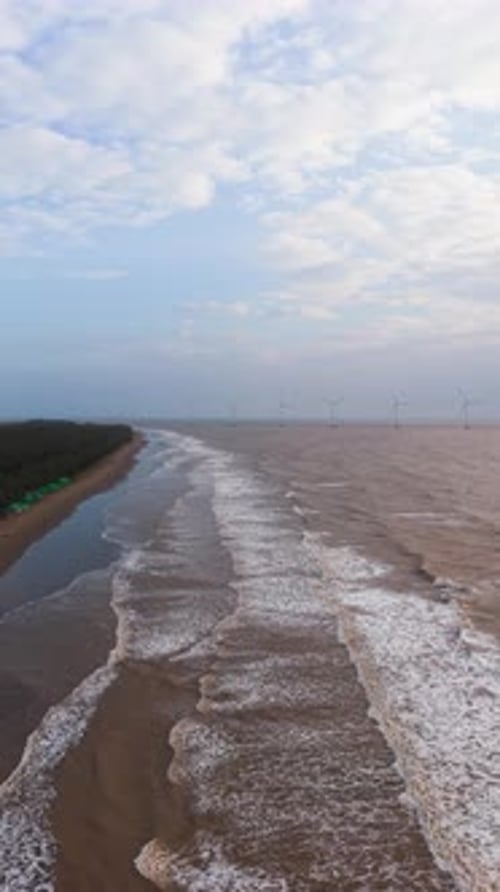 Coastal view of Tra Vinh in Vietnam with waves and wind turbines at sunrise.