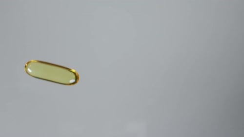 Yellow transparent capsule with fish oil or vitamin E, vitamin D tablet rolling into frame on flat