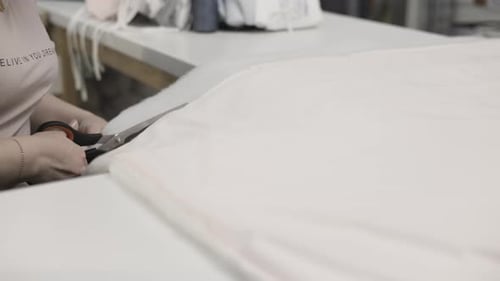 A Seamstress is Actively Cutting Fabric with a Pair of Scissors in a Textile Workshop
