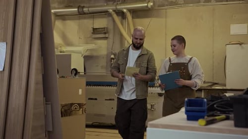 Two Coworkers Walking in Woodworking Workshop and Discussing Notes