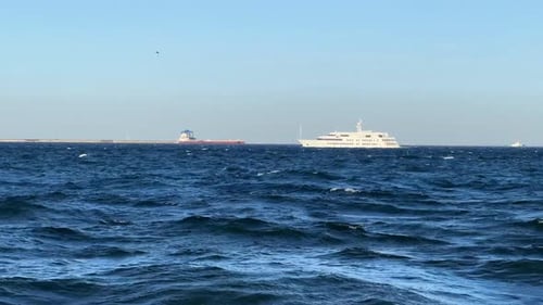 Luxury yacht sailing on the blue sea with waves and distant ships, sunny day