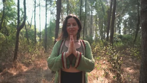 Women doing meditation in the forest with sun shinning through the trees.