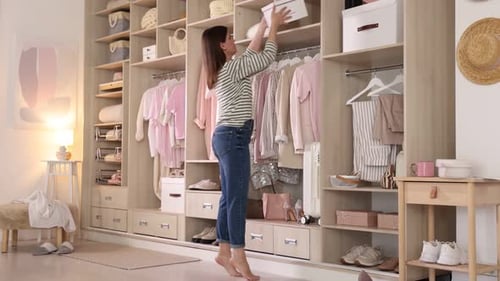 Femme mettant une boîte sur une étagère et choisissant une tenue dans une armoire à la maison
