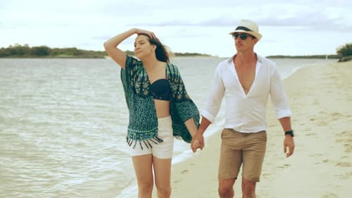 Couple Walking Along The Beach Holding Hands And Smiling Near Water In Australia. Medium Shot On ...