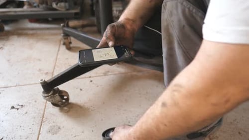Auto Mechanic Inspecting New Vehicle Part and Installation Instruction on Smartphone Repairman