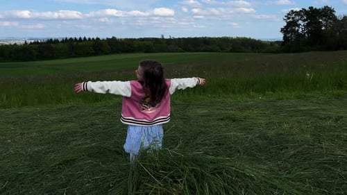A young little girl playing and falls on her back onto a pile of mowed grass in a field.