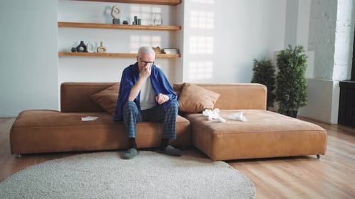 Elderly Sick Man Sitting on Couch in Cozy Home Interior Cough and Runny Nose Influenza or Pneumonia